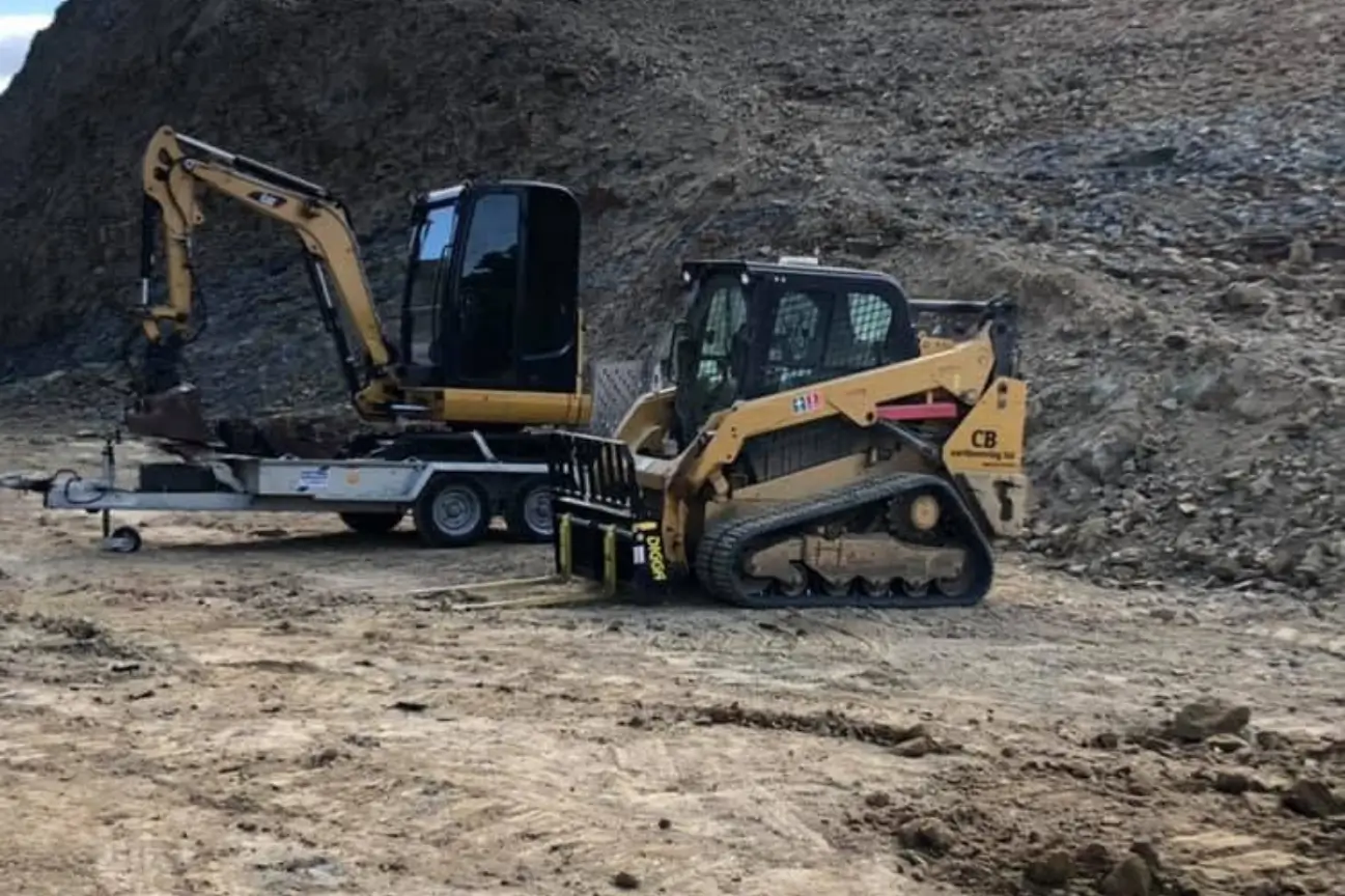 A tracked loader with fork attachment and a mini excavator on a trailer managed by CB Earthmoving Northland.