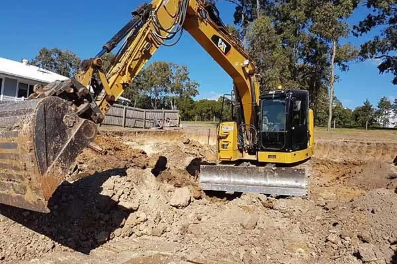 CAT excavator digging foundation trenches near a residential property for CB Earthmoving Northland.