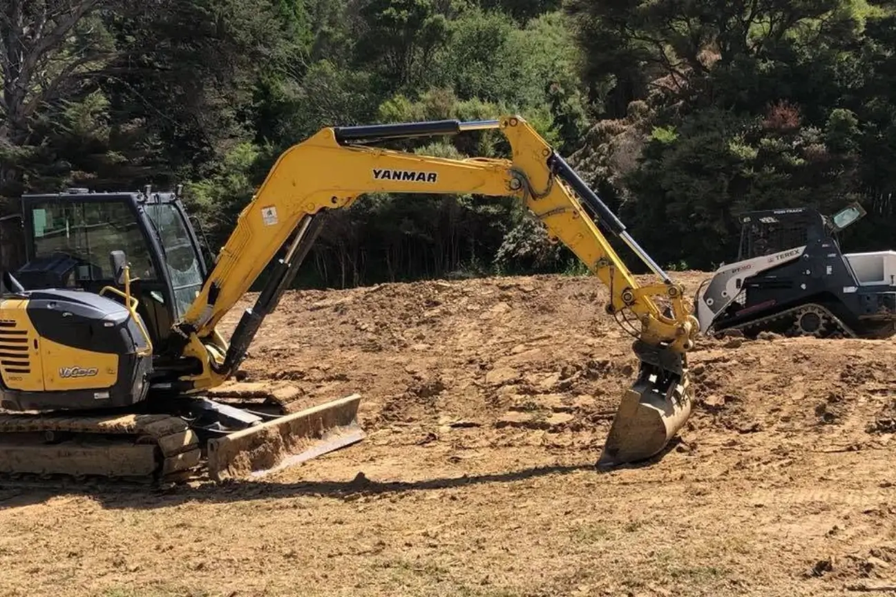 Yellow Yanmar excavator and track loader clearing earth on a project site managed by CB Earthmoving Northland.