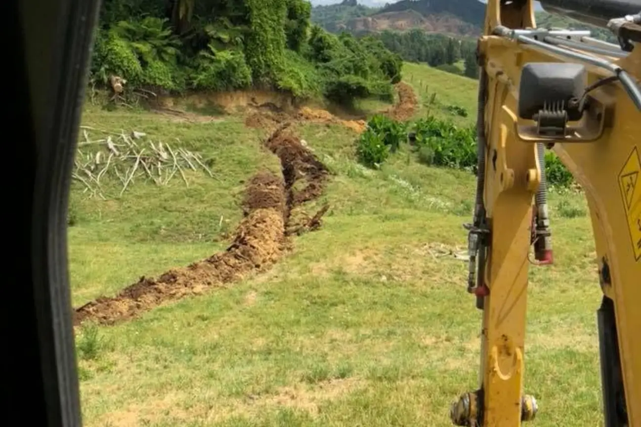 Long trench dug through a grassy hill by a CB Earthmoving Northland excavator for utility installation.