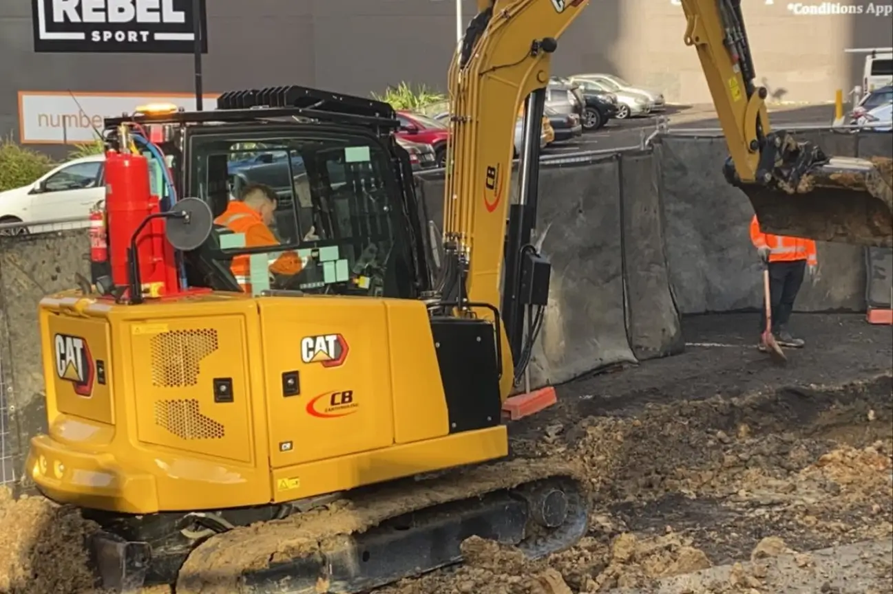 A yellow CAT excavator branded with CB Earthmoving Northland working on a site trenching and levelling project.