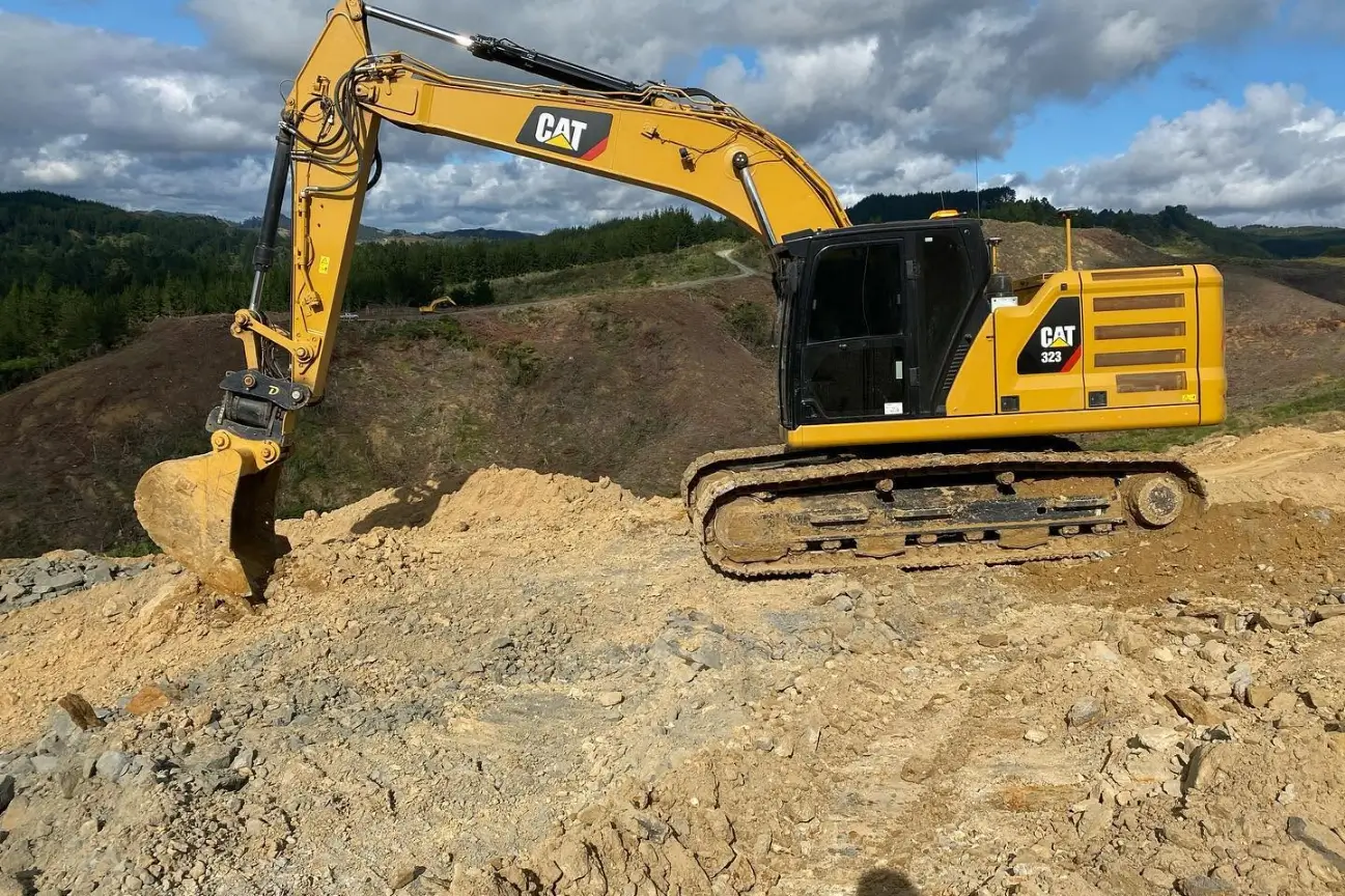 Large yellow CAT 323 excavator performing earth digging operations on a hillslope for CB Earthmoving Northland.