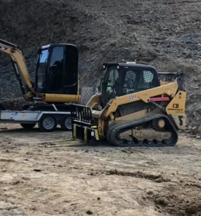 A tracked loader with fork attachment and a mini excavator on a trailer managed by CB Earthmoving Northland.