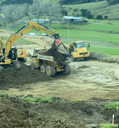 Heavy CAT excavator loading soil onto a dump truck on a rural site project managed by CB Earthmoving Northland.